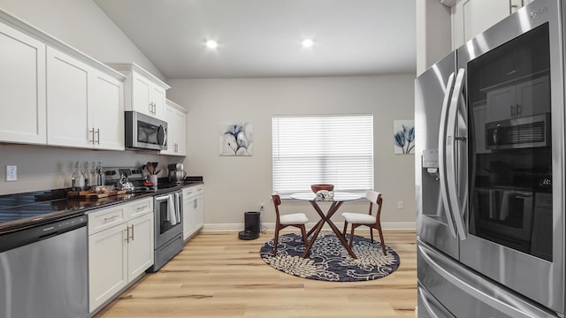 kitchen with dark countertops, light wood-style flooring, appliances with stainless steel finishes, and white cabinets