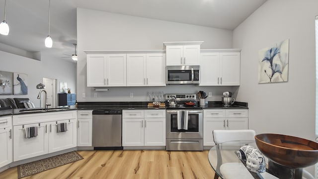 kitchen with stainless steel appliances, dark countertops, a sink, and hanging light fixtures