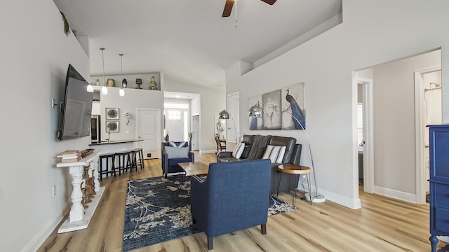 living area with high vaulted ceiling, ceiling fan, light wood-style flooring, and baseboards