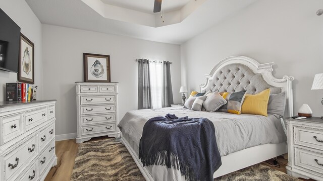 bedroom with light hardwood / wood-style flooring, ceiling fan, and a raised ceiling