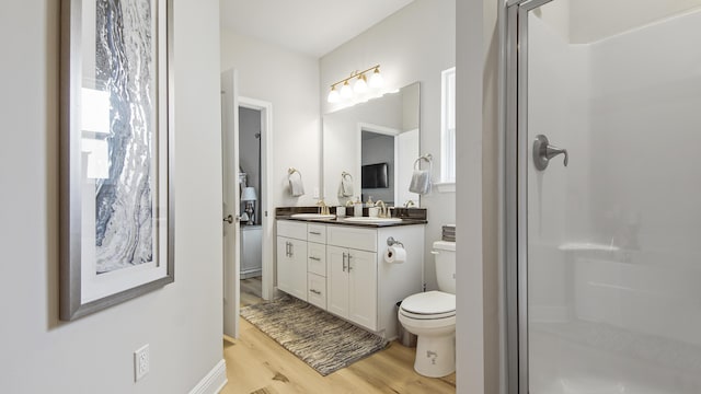 bathroom featuring a shower with shower door, toilet, wood finished floors, a sink, and double vanity