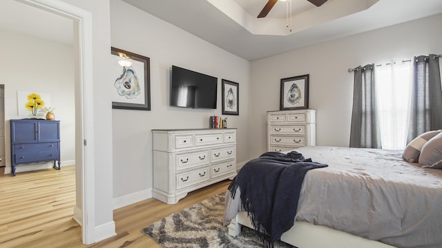 bedroom with light wood finished floors, ceiling fan, baseboards, and a tray ceiling