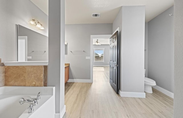 bathroom featuring a tub to relax in, toilet, vanity, ceiling fan, and hardwood / wood-style floors