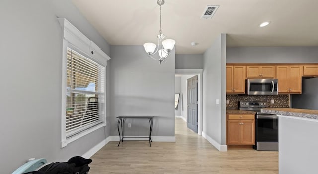 kitchen featuring tasteful backsplash, light wood-type flooring, appliances with stainless steel finishes, a notable chandelier, and pendant lighting