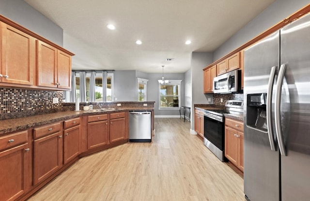 kitchen with stainless steel appliances, hanging light fixtures, a healthy amount of sunlight, light hardwood / wood-style floors, and backsplash