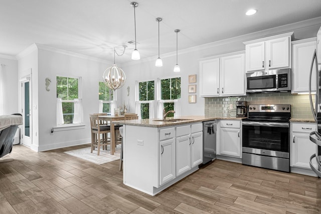 kitchen with appliances with stainless steel finishes, sink, kitchen peninsula, hanging light fixtures, and ornamental molding