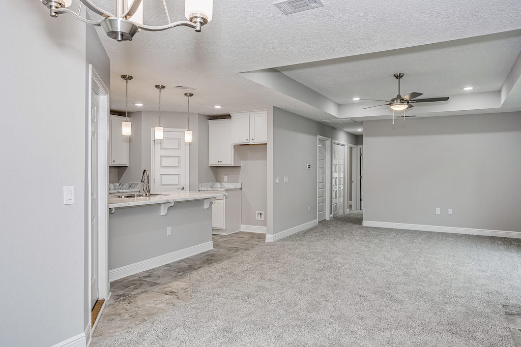 kitchen featuring light carpet, hanging light fixtures, a raised ceiling, a kitchen breakfast bar, and white cabinetry