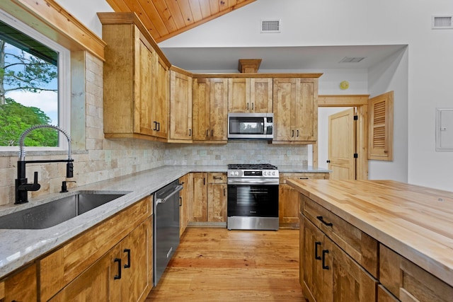 kitchen with lofted ceiling, sink, appliances with stainless steel finishes, backsplash, and light stone countertops