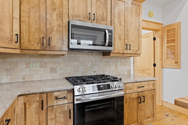 kitchen featuring backsplash, light stone countertops, stainless steel appliances, and light hardwood / wood-style flooring