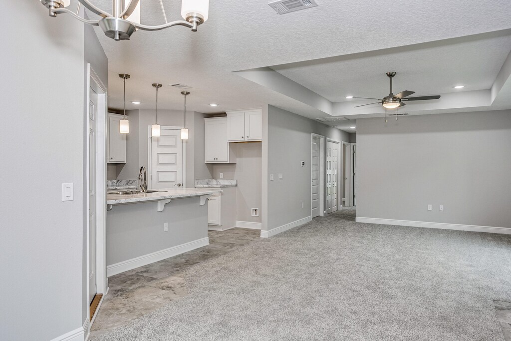 kitchen with light carpet, a kitchen bar, pendant lighting, a raised ceiling, and white cabinetry