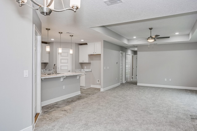 kitchen with light carpet, a kitchen bar, pendant lighting, a raised ceiling, and white cabinetry