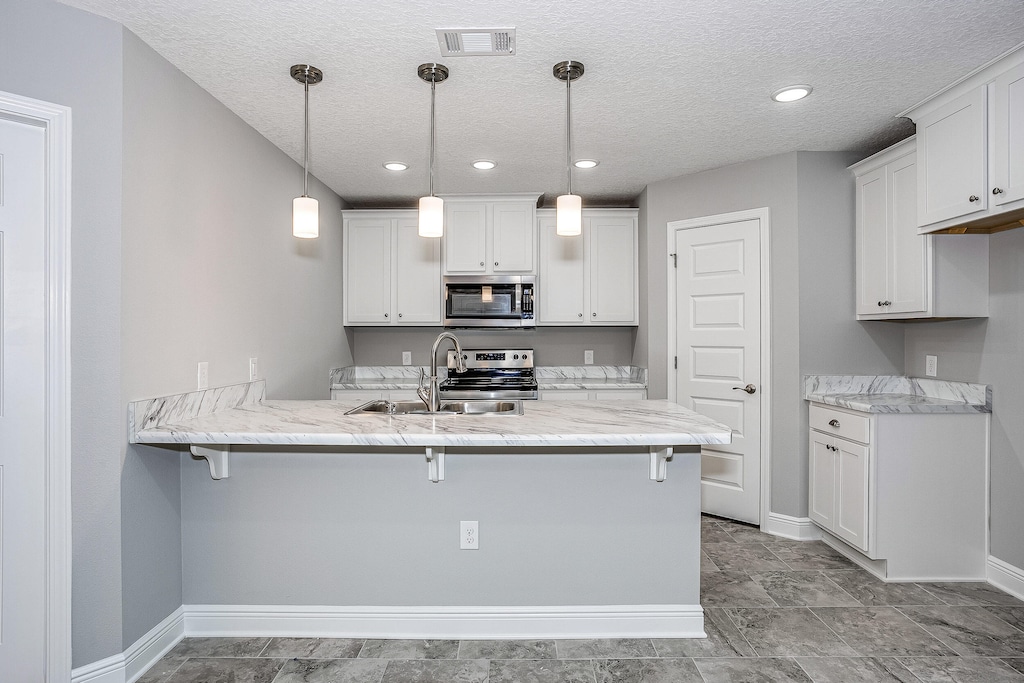 kitchen featuring sink, kitchen peninsula, stainless steel appliances, decorative light fixtures, and white cabinets