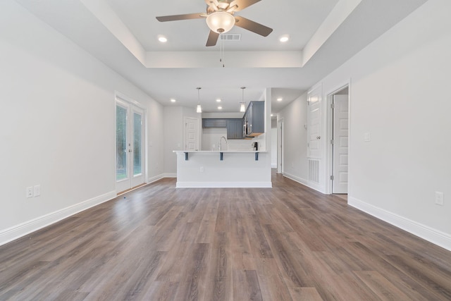 unfurnished living room featuring french doors, dark hardwood / wood-style floors, a tray ceiling, and ceiling fan