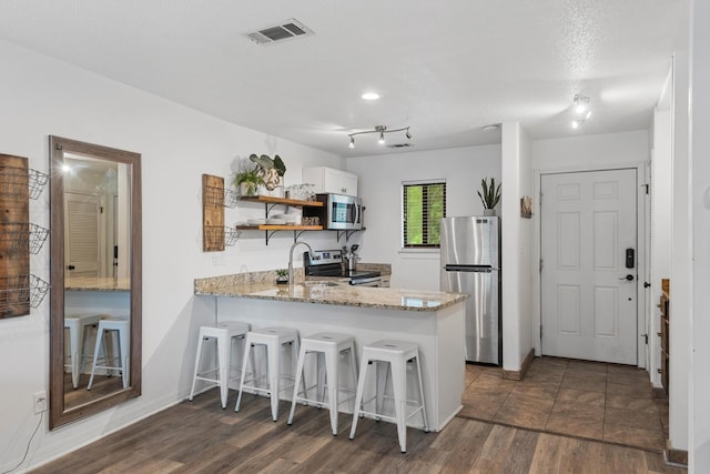 kitchen with kitchen peninsula, appliances with stainless steel finishes, a kitchen bar, sink, and white cabinetry