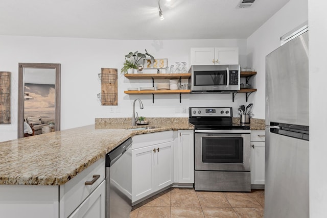 kitchen with sink, stainless steel appliances, light stone counters, kitchen peninsula, and white cabinets