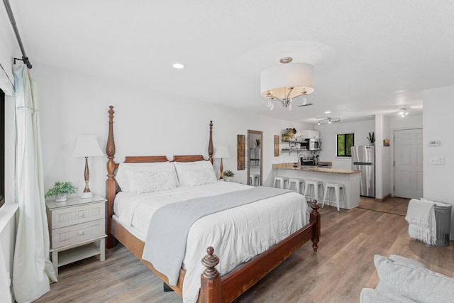 bedroom featuring stainless steel refrigerator, sink, an inviting chandelier, and light wood-type flooring