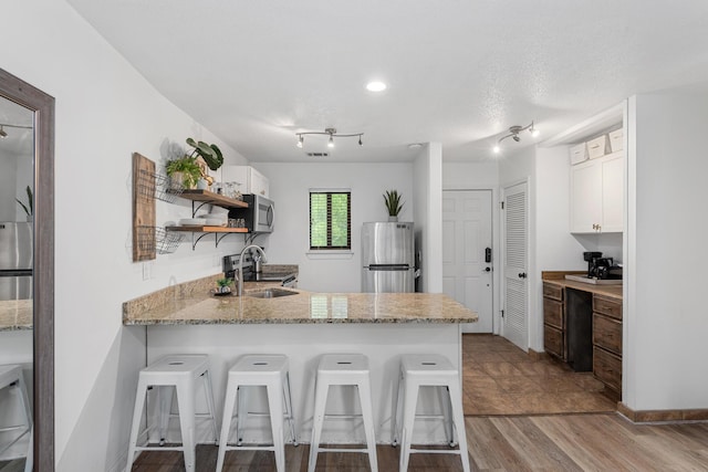 kitchen with white cabinetry, kitchen peninsula, a breakfast bar, appliances with stainless steel finishes, and light wood-type flooring