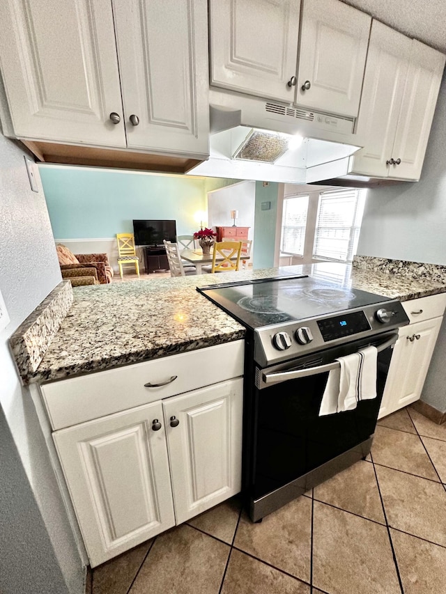 kitchen with under cabinet range hood, stainless steel electric stove, white cabinets, and light tile patterned flooring