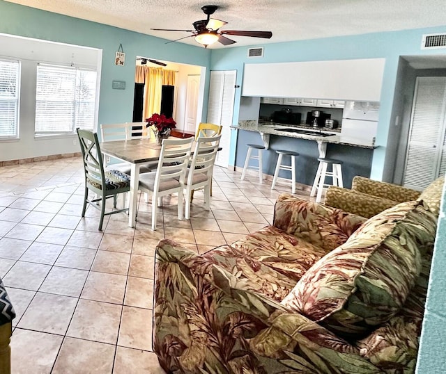 dining room featuring a textured ceiling, light tile patterned flooring, visible vents, baseboards, and a ceiling fan