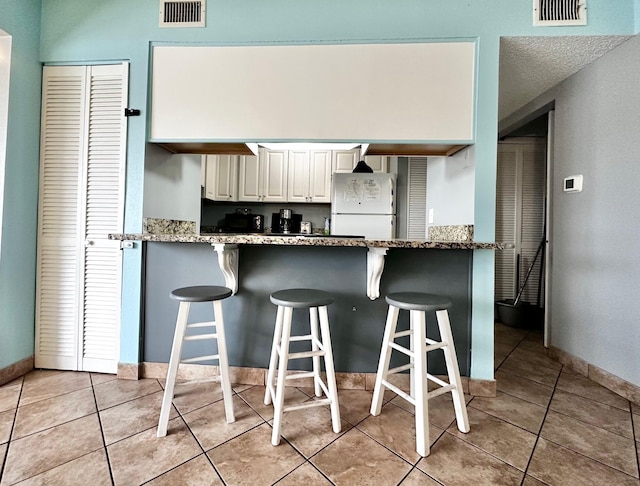 kitchen with light stone countertops, visible vents, white cabinets, and freestanding refrigerator