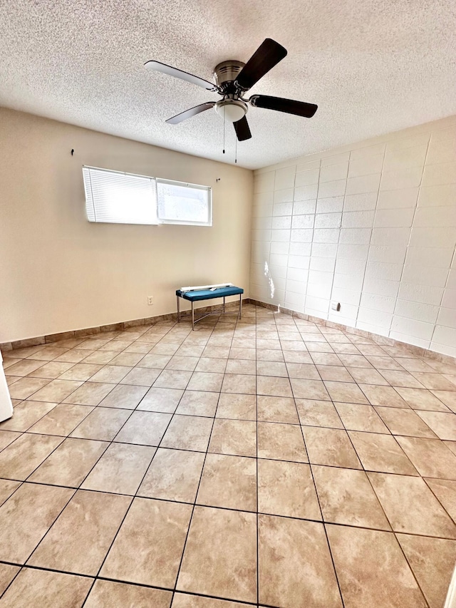 empty room with light tile patterned floors, baseboards, a ceiling fan, and a textured ceiling