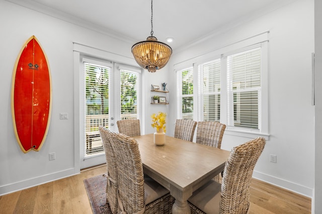 dining area with crown molding, a notable chandelier, and light wood-type flooring