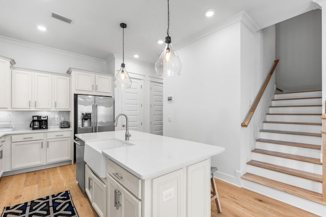 kitchen with appliances with stainless steel finishes, sink, white cabinets, hanging light fixtures, and a kitchen island with sink