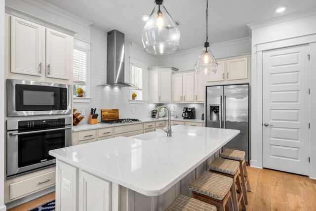 kitchen with sink, a breakfast bar area, appliances with stainless steel finishes, a center island with sink, and wall chimney exhaust hood