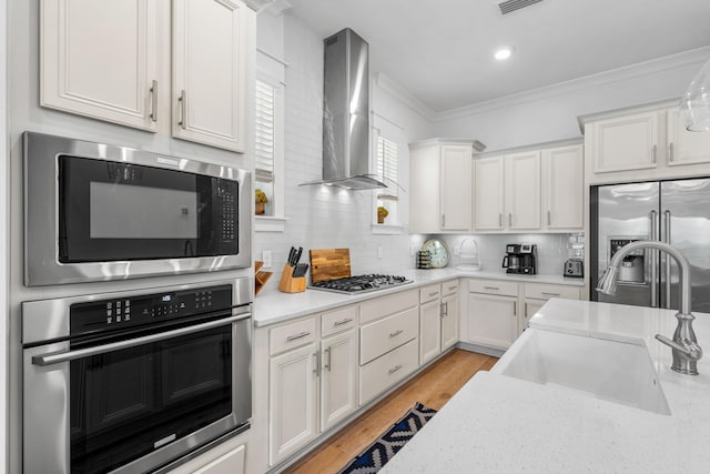 kitchen featuring wall chimney exhaust hood, white cabinetry, appliances with stainless steel finishes, and sink