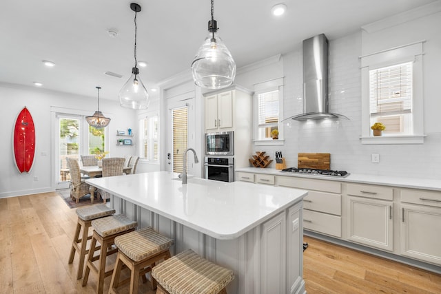 kitchen with a center island with sink, appliances with stainless steel finishes, wall chimney range hood, and a kitchen breakfast bar