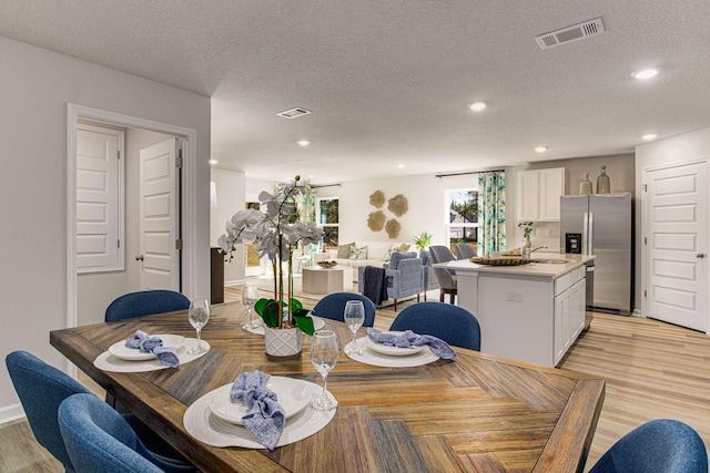 dining space with sink, a textured ceiling, and light hardwood / wood-style flooring