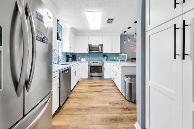 kitchen with white cabinetry, sink, stainless steel appliances, pendant lighting, and a textured ceiling