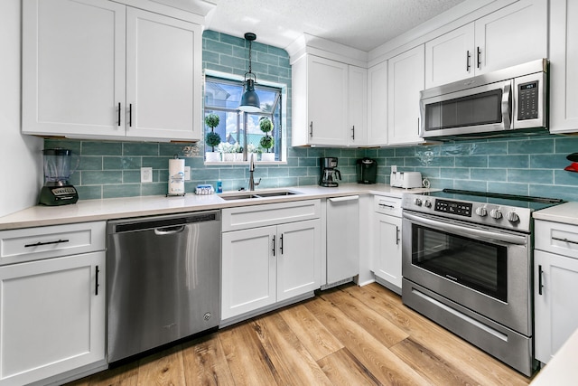 kitchen featuring sink, white cabinetry, hanging light fixtures, and appliances with stainless steel finishes