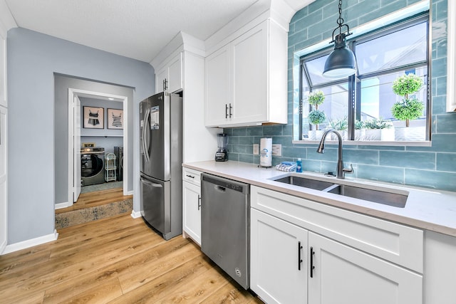 kitchen with appliances with stainless steel finishes, sink, separate washer and dryer, light hardwood / wood-style flooring, and white cabinets