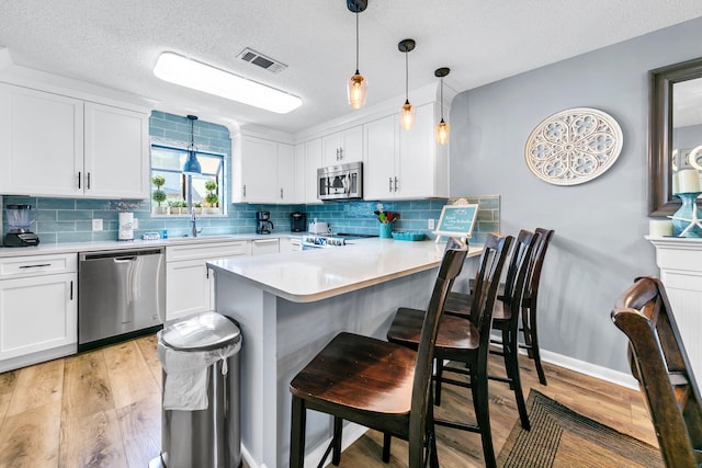 kitchen featuring white cabinetry, stainless steel appliances, a kitchen breakfast bar, pendant lighting, and light wood-type flooring