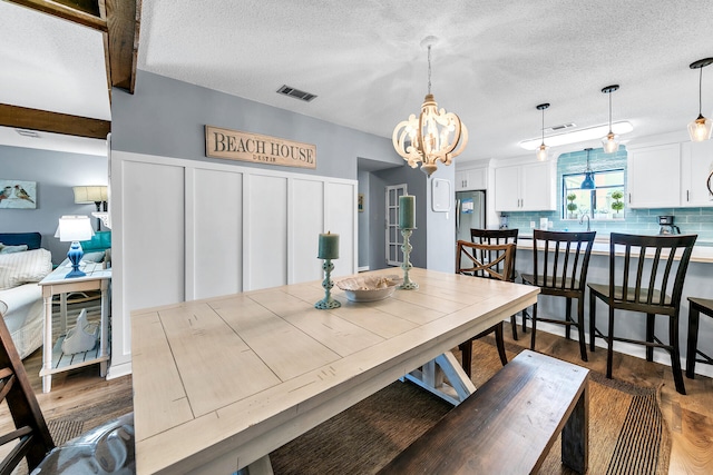 dining room with dark hardwood / wood-style flooring, beamed ceiling, a textured ceiling, and a notable chandelier