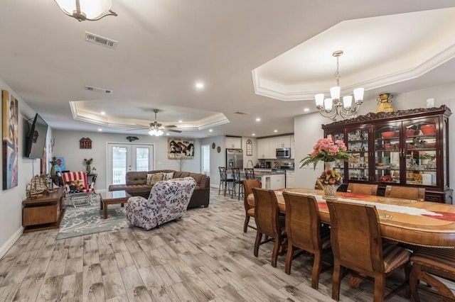 dining area featuring ceiling fan with notable chandelier, french doors, light wood-type flooring, and a tray ceiling