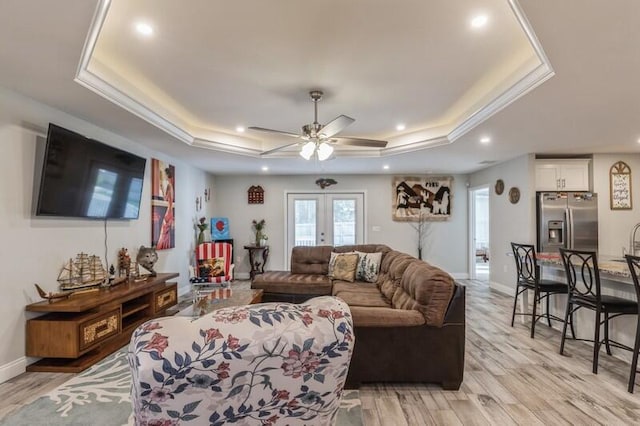 living room with a tray ceiling, french doors, light wood-type flooring, ceiling fan, and ornamental molding