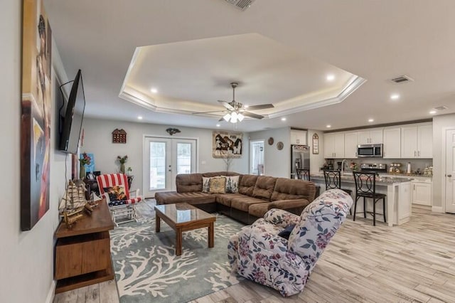 living room featuring french doors, ceiling fan, a raised ceiling, and light hardwood / wood-style floors