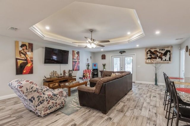 living room with a raised ceiling, french doors, light hardwood / wood-style flooring, and ceiling fan