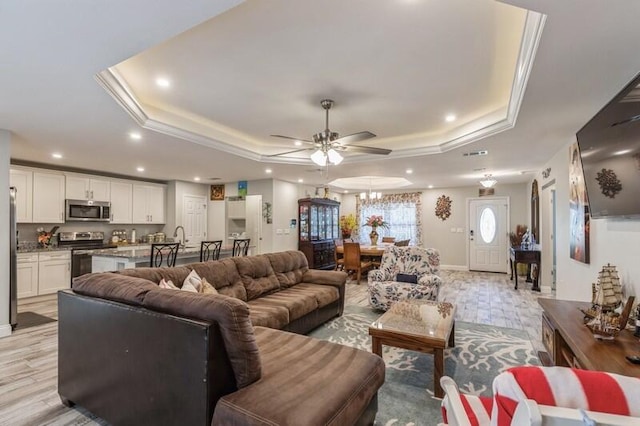 living room featuring crown molding, ceiling fan, light wood-type flooring, and a tray ceiling