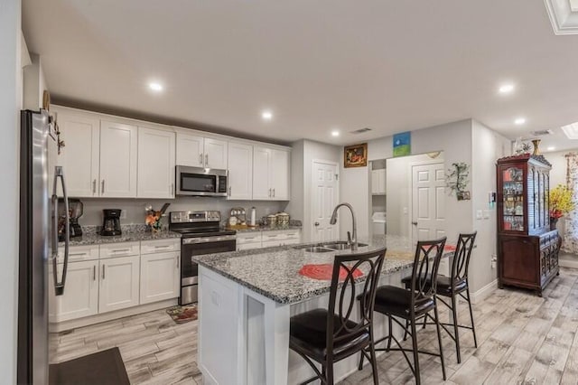 kitchen with a kitchen island with sink, sink, appliances with stainless steel finishes, and light wood-type flooring