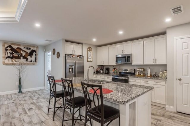 kitchen with white cabinetry, an island with sink, sink, light hardwood / wood-style floors, and appliances with stainless steel finishes