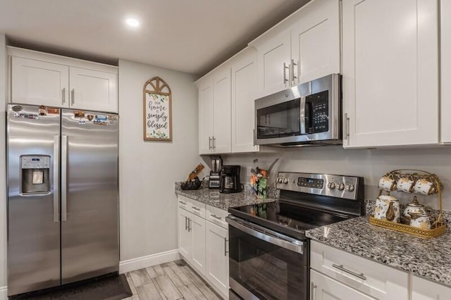 kitchen featuring appliances with stainless steel finishes, light hardwood / wood-style flooring, white cabinetry, and light stone counters