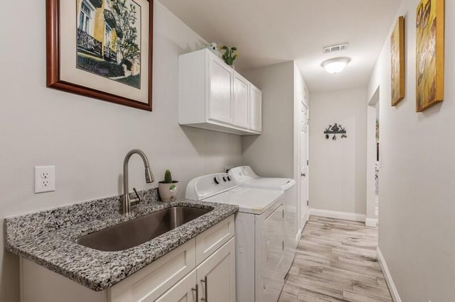 clothes washing area featuring cabinets, washing machine and dryer, light hardwood / wood-style flooring, and sink