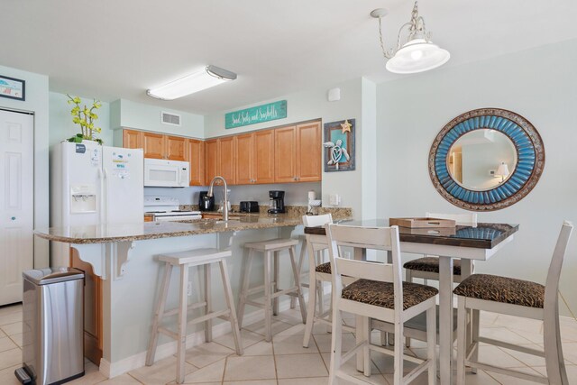 kitchen featuring pendant lighting, white appliances, light stone counters, and light tile patterned floors