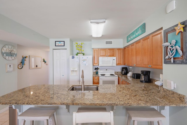 kitchen featuring white appliances, a kitchen breakfast bar, sink, light stone counters, and kitchen peninsula