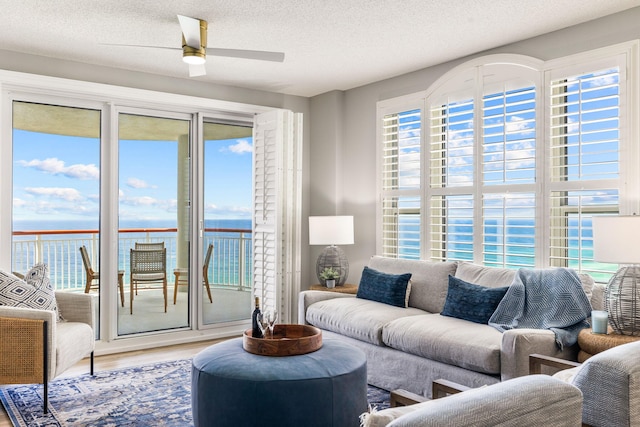 living room with a textured ceiling, a water view, hardwood / wood-style floors, and ceiling fan