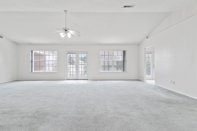 carpeted empty room featuring plenty of natural light, lofted ceiling, a textured ceiling, and french doors