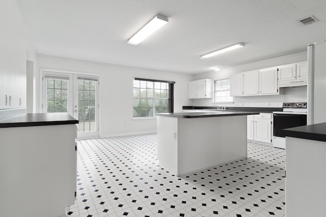 kitchen featuring electric range oven, a textured ceiling, white cabinets, and a kitchen island